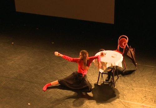 Astrid Julen dancing at a table with a cup in her choreography T-Raum.